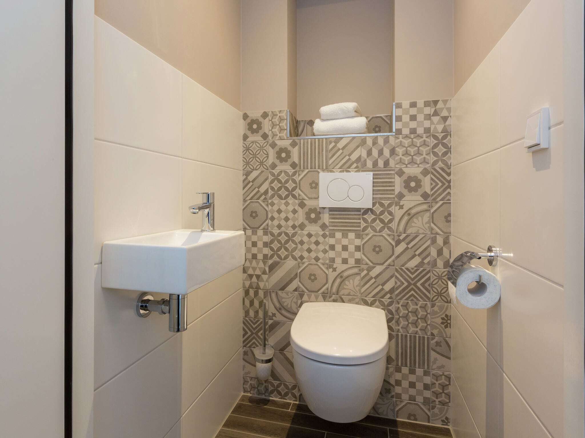 Ein kleines, modernes Badezimmer mit Waschbecken, Toilette und gemusterten Fliesen.