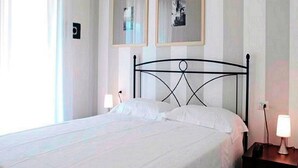 A neatly made bed in a room with two framed pictures on the wall, a bedside lamp, and a window with curtains. - Apartment in Tuscany Near Chianti Vineyards (Barberino Tavarnelle)