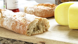Een brood op een houten snijplank, een pot jam en een stokbrood.