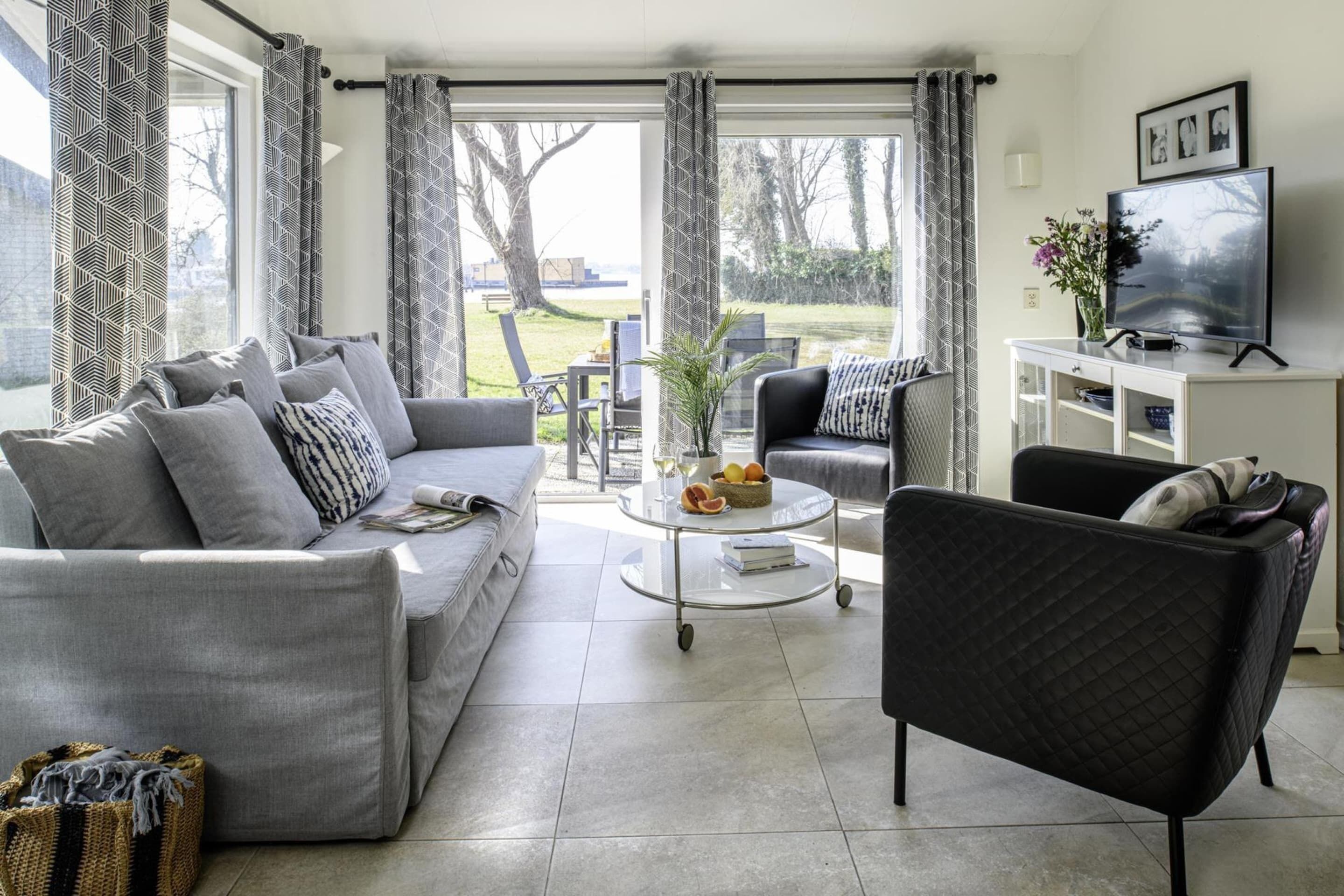 A living room with a grey sofa, a black armchair, a glass coffee table, and a TV on a white stand.