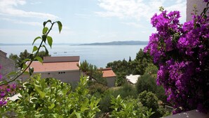 Un balcón con vista a un cuerpo de agua, rodeado de follaje y flores moradas.