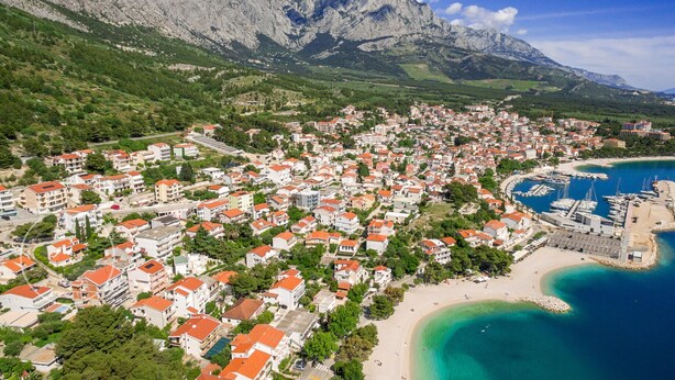 Vista aérea de un pueblo costero con edificios residenciales, un puerto deportivo y una playa.