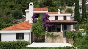 Una casa de dos pisos con techo de tejas rojas, paredes blancas y cimientos de piedra.