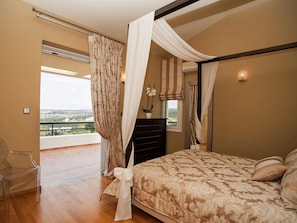 A bedroom with a large bed, a view of the outdoors, and a balcony.