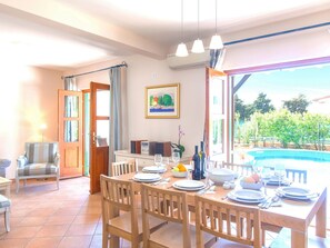 A dining area with a table set for four, chairs, a painting on the wall, and a view of a swimming pool outside. - Beautiful Villa With Spacious Terrace and Private Swimming Pool, on the Croatian Island of Hvar (Hvar)