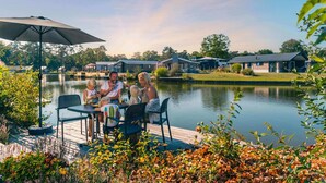 A family dining at a lakeside deck with a view of the lake and nearby cabins. - Comfortable Chalet in the Green Kempen (Mol)