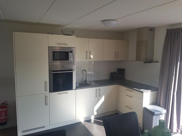 A modern kitchen with white cabinets, a built-in oven, microwave, and a coffee maker. - Comfortable Chalet in the Green Kempen (Mol)
