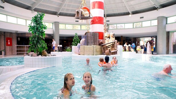 An indoor swimming pool with a central fountain, surrounded by a tiled deck and potted plants. - Comfortable Chalet in the Green Kempen (Mol)