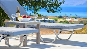 A sun lounger with a table set for a meal, overlooking a coastal view. - New Beautiful Villa With Private Pool at Coastal Area Just Outside Rethymno, NW (Apokoronas)