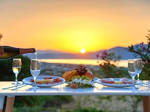 A table set for a meal with plates of food, a bottle of wine, and glasses, overlooking a sunset over a body of water. - New Beautiful Villa With Private Pool at Coastal Area Just Outside Rethymno, NW (Apokoronas)