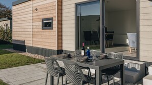 Un espace de repas extérieur moderne, avec une table et des chaises, une porte vitrée donnant sur l’intérieur et une petite fenêtre sur le mur extérieur.