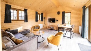 Accogliente interno di una baita in legno con divano, poltrone, tavolo da pranzo e televisore.