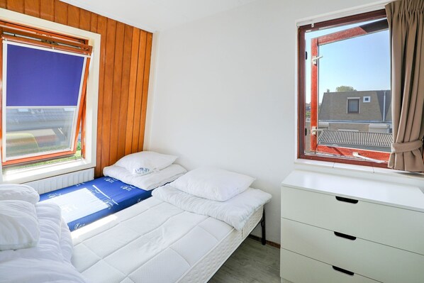 Une chambre avec deux lits, une fenêtre avec des rideaux, une commode blanche et une vue sur les bâtiments environnants.