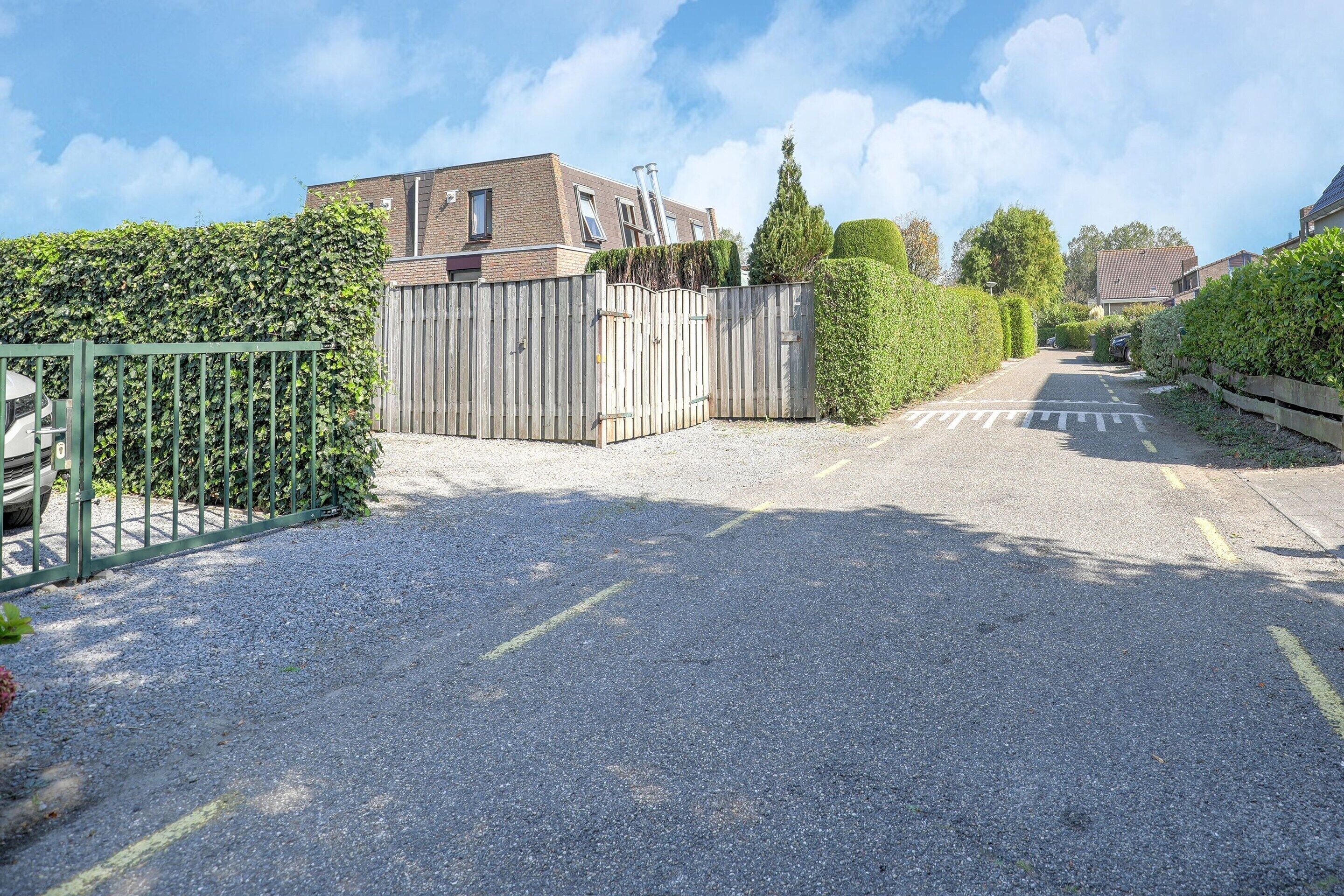 Une allée menant à une maison, avec une clôture en bois et un portail vert.