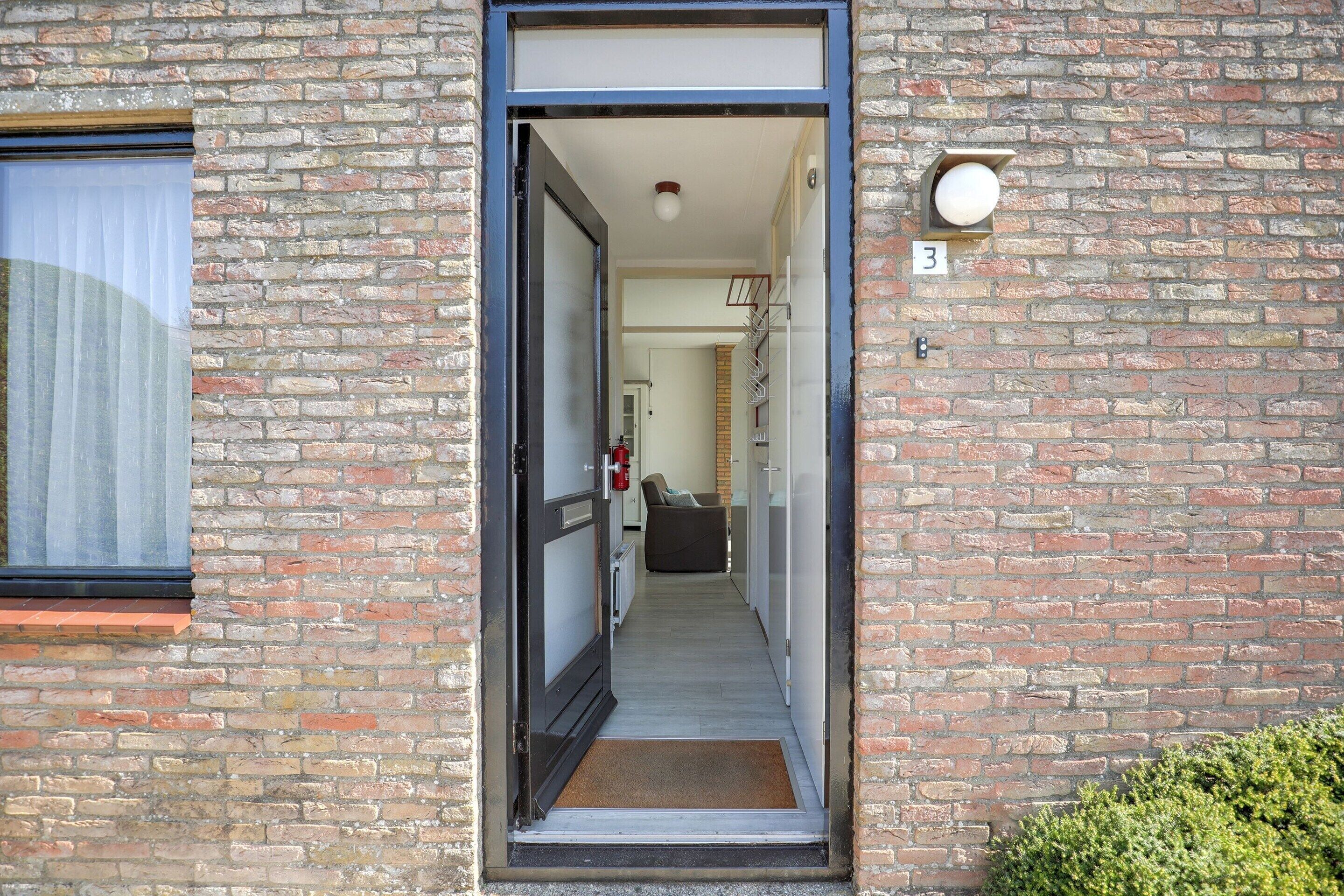 A narrow entrance to a brick building with a door, a doormat, and a number '3' sign on the wall.