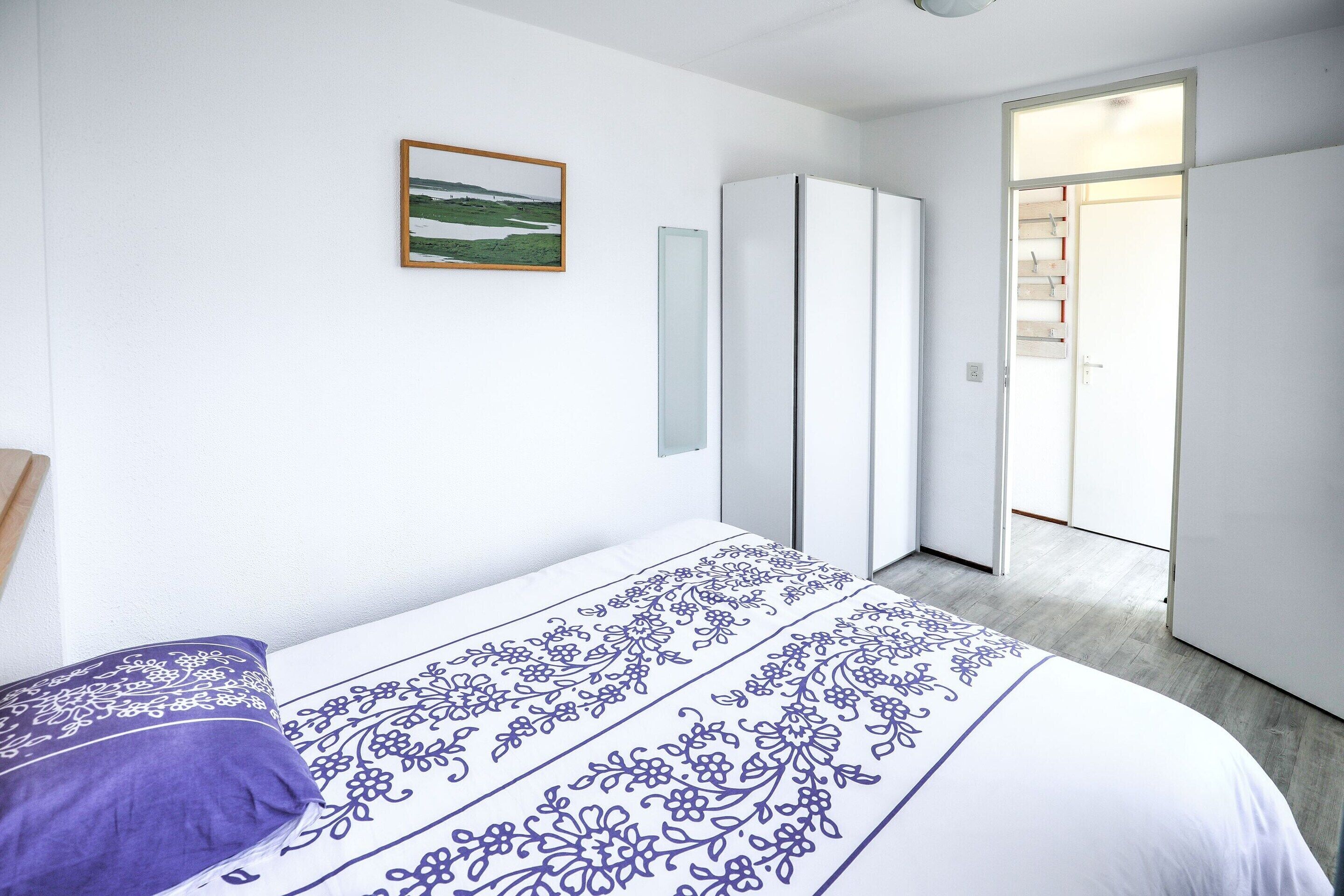 Une chambre à coucher comprenant un lit, une armoire, une porte donnant sur une autre pièce et un tableau encadré accroché au mur.