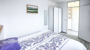 Une chambre à coucher comprenant un lit, une armoire, une porte donnant sur une autre pièce et un tableau encadré accroché au mur.