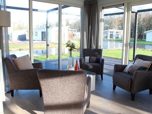 A modern living room with large windows, two sofas, a coffee table, and a vase with flowers. - Luxury Villa With Three Bathrooms, Near a National Park (IJhorst)