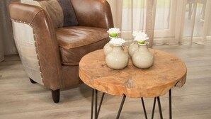 A brown leather sofa with a throw blanket, a wooden coffee table with two ceramic vases, and sheer curtains in a room with wooden flooring. - Luxury Villa With Three Bathrooms, Near a National Park (IJhorst)