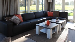 A modern living room with a black sectional sofa, a white coffee table, and a view of a green landscape through large windows. - Luxury Villa With Three Bathrooms, Near a National Park (IJhorst)