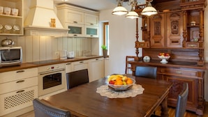 A kitchen with white cabinets, a wooden dining table with a fruit bowl, and a vintage-style chandelier. - Villa in Sumartin Near the Beach & Ferry Port (Selca)