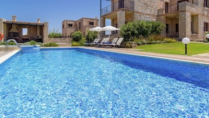 Une piscine entourée de bâtiments en pierre dotés de balcons, avec des chaises longues et des parasols à proximité.