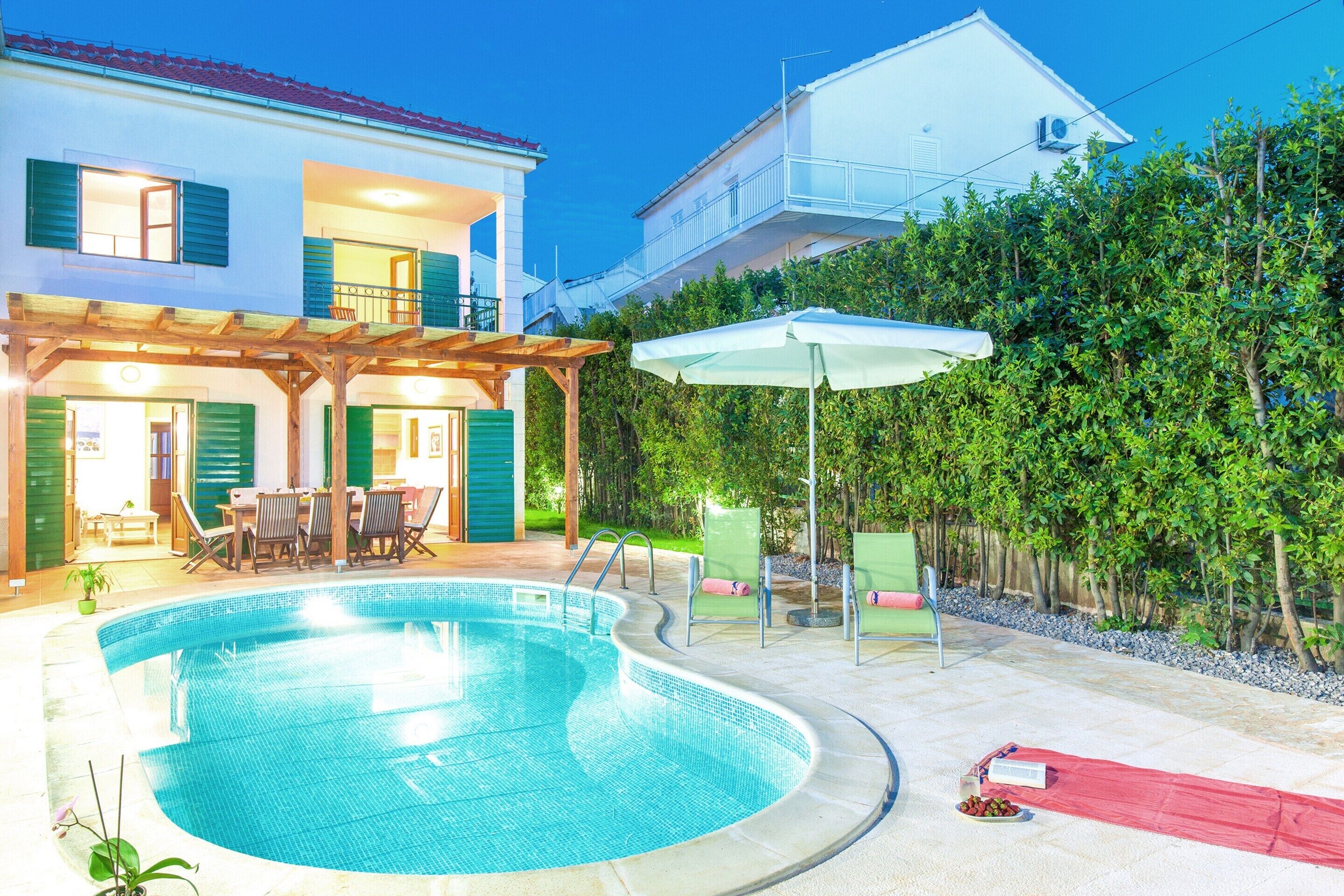 Ein Schwimmbad mit Holzterrasse, Gartenmöbeln und einer überdachten Sitzecke.