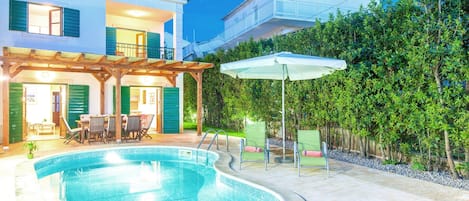 Piscina com deck de madeira, mobiliário de exterior e área de estar coberta.