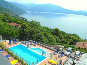 A swimming pool with lounge chairs, surrounded by greenery and a view of a lake and mountains. - Spacious Apartment in Rancone With Lake View (Oggebbio)