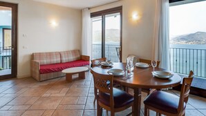 A balcony with a dining table set for two, a sofa, and a view of the sea. - Residential Complex With Panoramic Views and Pool (Oggebbio)