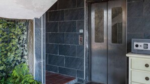 An elevator with a metallic door and a control panel, surrounded by dark stone walls and a green plant wall. - Residential Complex With Panoramic Views and Pool (Oggebbio)