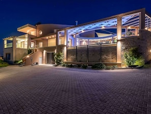A modern multi-story building with a spacious entrance, a covered outdoor area, and a well-lit facade. - Luxury Villa With Heated Pool in Agia Pelagia (Malevizi)