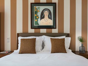 A hotel room with a bed, two brown pillows, a framed artwork above the bed, and a small plant on the nightstand.
