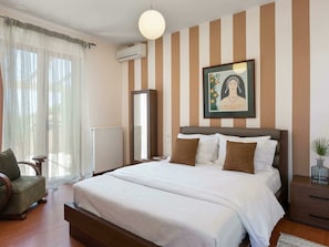 A bedroom with a large bed, a chair, a bedside table, a radiator, and a painting on the wall. - Luxury Villa With Heated Pool in Agia Pelagia (Malevizi)