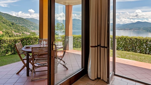 A balcony with a table and chairs, a glass door, and a view of a lake and mountains. - Residential Complex With Panoramic Views and Pool (Oggebbio)