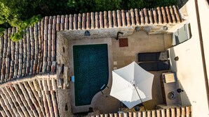 Luftaufnahme eines Poolbereichs auf einem Dach mit einem rechteckigen Pool, einem weißen Sonnenschirm und einer Sitzgelegenheit mit Tisch und Stühlen.