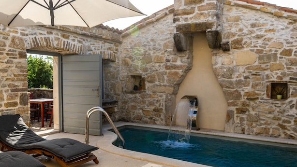 Ein Gebäude aus Stein mit Pool, Liegestühlen und einem Wasserspiel.