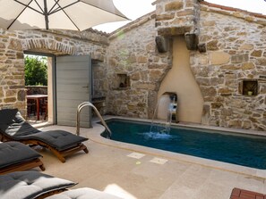Ein Gebäude aus Stein mit Pool, Liegestühlen und einem Wasserspiel.