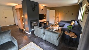 A modern living room with a fireplace, grey sofas, a coffee table, and a TV. - Modern Apartment in Belgium With Bubble Bath (Durbuy)