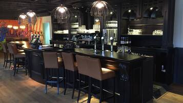 Een bar met een lange toonbank, meerdere stoelen en hangende hanglampen.