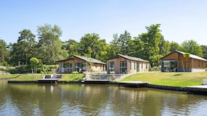Una propiedad junto al lago con tres cabañas de madera, cada una con terraza y un pequeño jardín.