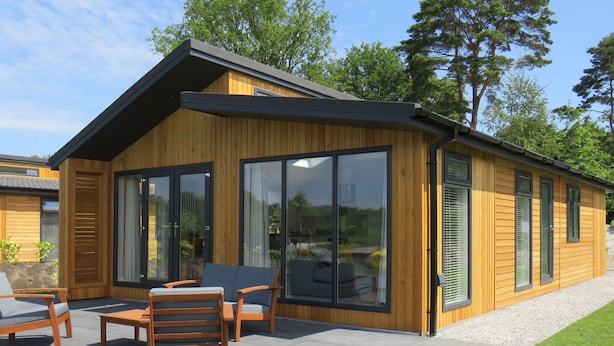 Una casa moderna de madera con grandes puertas correderas de vidrio, un patio con mobiliario exterior y un césped bien cuidado.