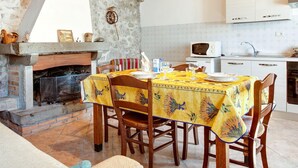 A rustic kitchen with a stone wall, wooden beams, a fireplace, and a dining table set for four. - Farmhouse in Italy With Private Terrace (Bagni di Lucca)