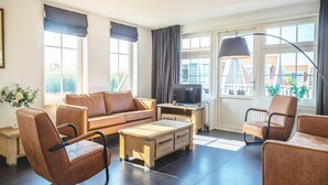 A modern living room with a leather sofa, a wooden coffee table, a TV, and large windows with curtains. - Holiday Home Built in Zaanse Style, Near Alkmaar (West-Graftdijk)