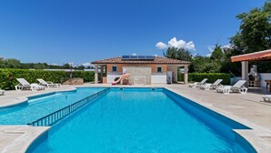 En swimmingpool med liggestole, en lille bygning med et tagtækket tag og et grillområde.