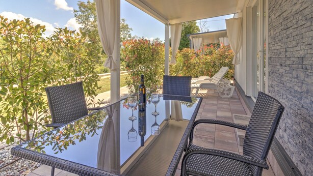 An outdoor patio with wicker chairs, a glass table, and a bottle of wine. - Mobile Home in Banjole Near the Beach (Medulin)