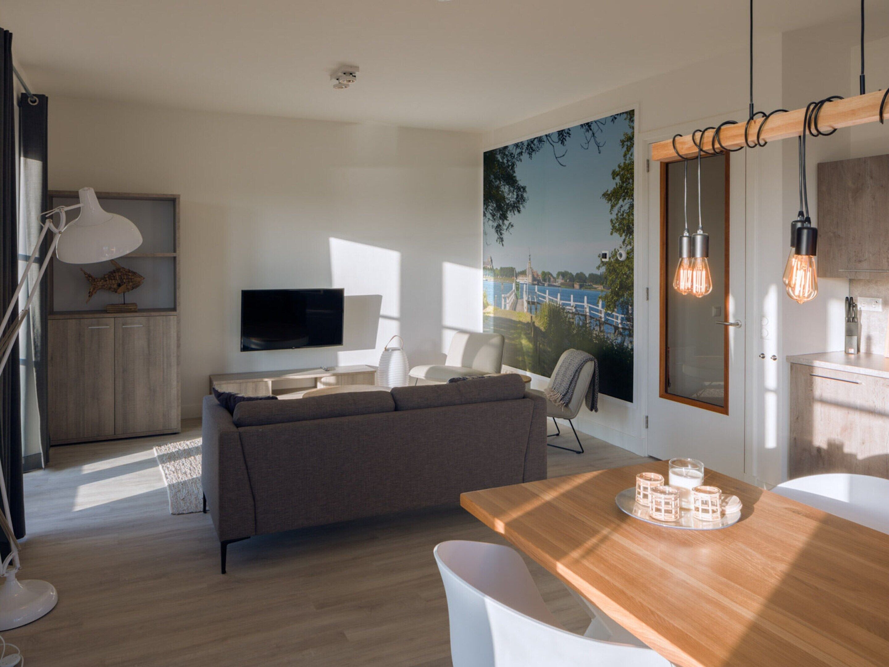 A modern living room with a sofa, a dining table with glasses, and a TV.