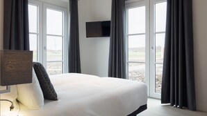 A bedroom with a bed, a TV mounted on the wall, and large windows with curtains. - Modern Apartment 2 Bath Rooms, Close to Lake Veere (Kamperland)