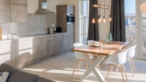 A modern kitchen with a dining area, featuring a wooden table, white chairs, and a large window with curtains. - Modern Apartment 2 Bath Rooms, Close to Lake Veere (Kamperland)