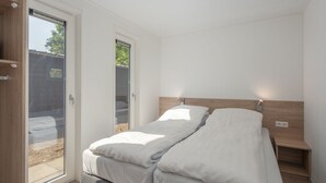 A modern bedroom with a bed, a nightstand, a wooden headboard, and a sliding glass door leading to an outdoor area. - Modern Lodge With Infrared Sauna, Near Helmond (Mierlo)